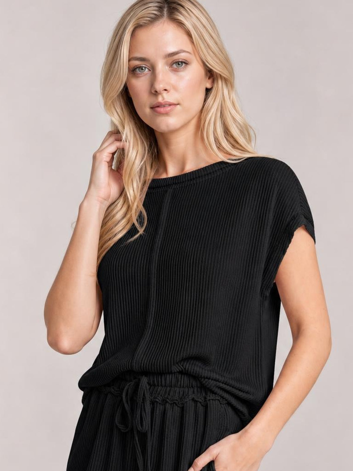 A model poses in a black ribbed top and pants set, featuring a relaxed short-sleeve silhouette, elastic drawstring waist, and hand resting near her hair.