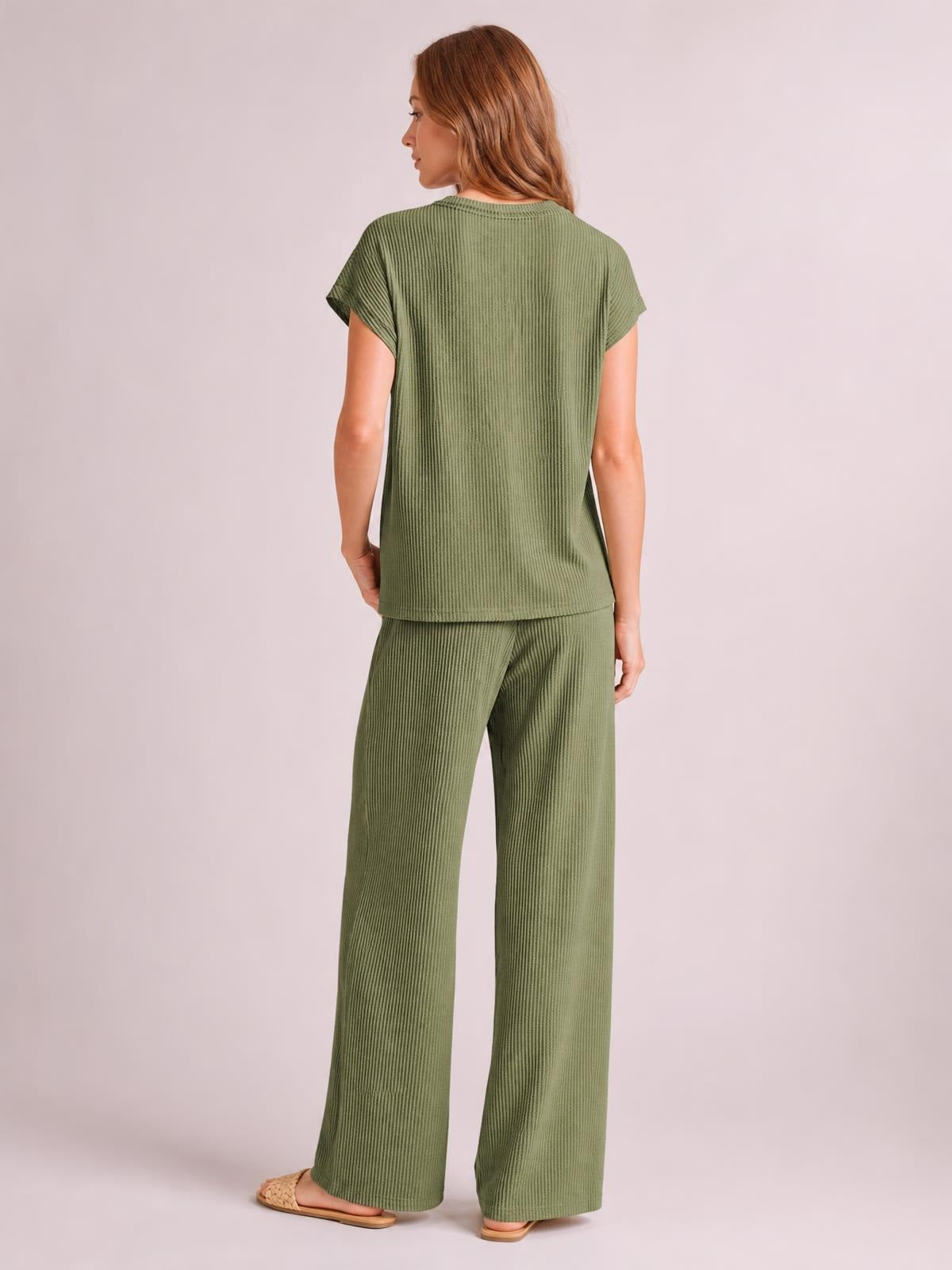 Model turned slightly away wears an olive-green ribbed top with short sleeves and wide-leg pants, showing a relaxed, streamlined silhouette.