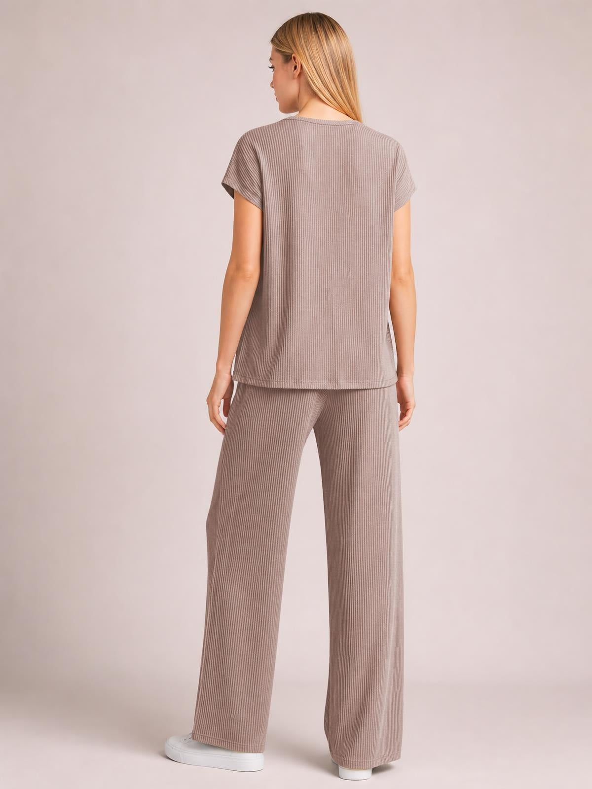 Model stands facing away in a taupe ribbed top and wide-leg pants set, featuring short sleeves and exposed seam detailing for a relaxed silhouette.