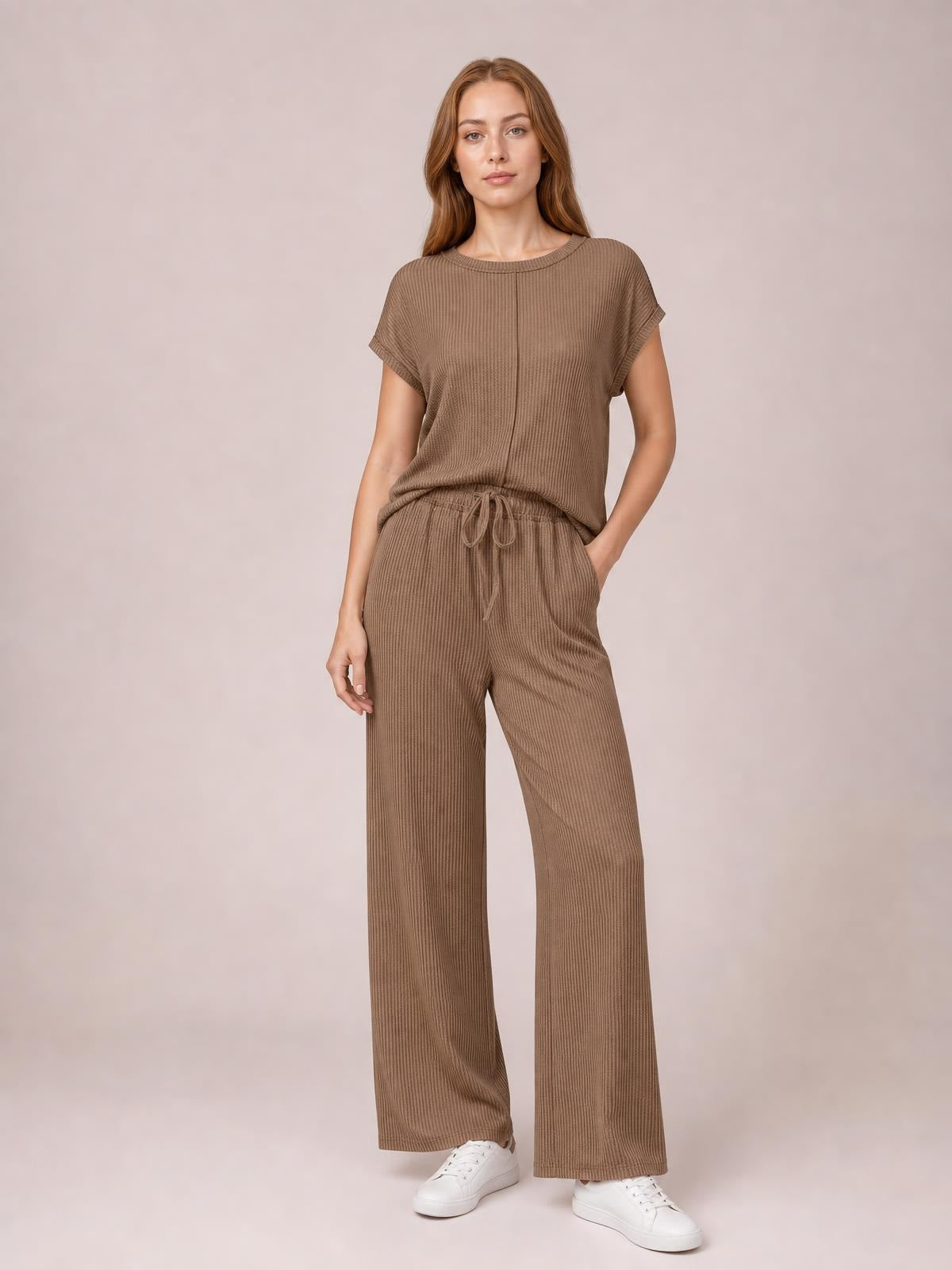Model stands in a brown ribbed top and wide-leg pants set with exposed center seams, short sleeves, drawstring waist, and one hand in a pocket.