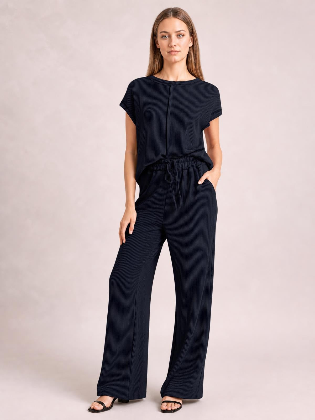 Model poses in a dark navy ribbed top and wide-leg pants set with short sleeves, an exposed center seam, and an elastic drawstring waist.