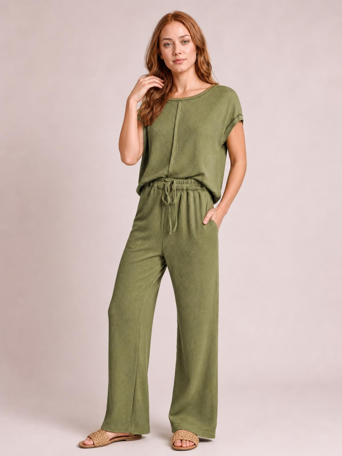 Model poses in a sage green ribbed top and wide-leg pants set with exposed seams, short sleeves, an elastic drawstring waist, and relaxed silhouette.
