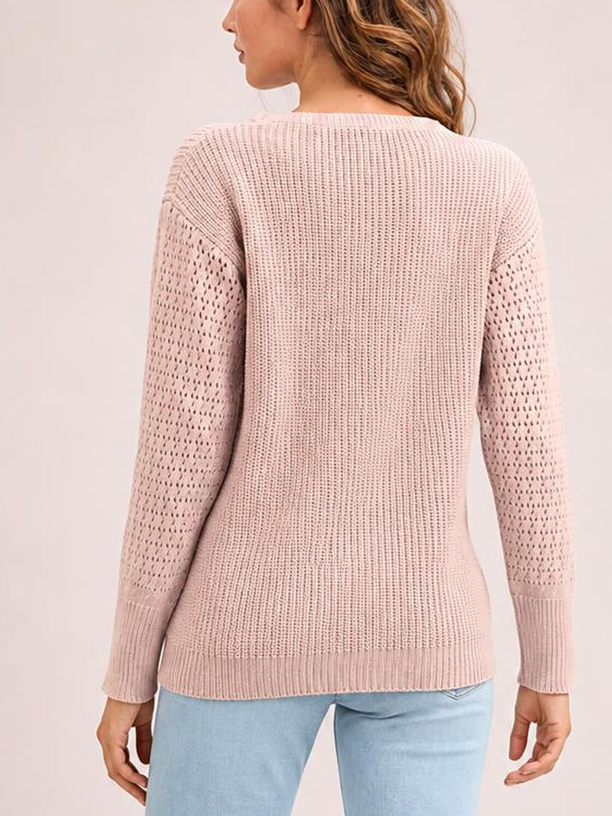 Model shown from the back wearing a blush pink ribbed pullover sweater with a round neck, dropped shoulders, openwork long sleeves, and a regular silhouette.