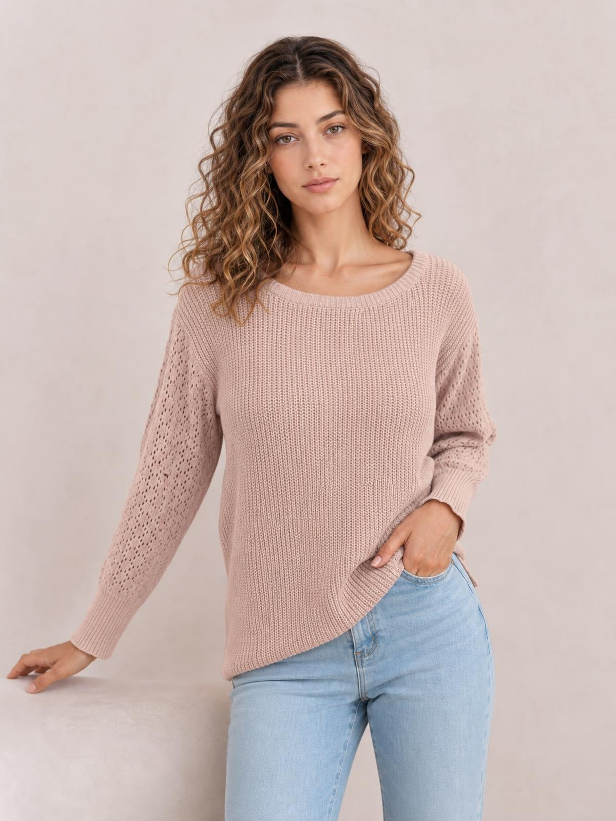 Model in a soft blush ribbed pullover sweater with a round neck, dropped shoulders, long openwork sleeves, and a relaxed regular-length silhouette.
