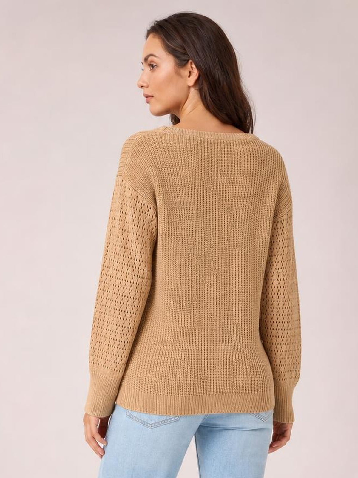 Model shown from the back in a camel ribbed round-neck pullover sweater with openwork long sleeves, dropped shoulders, and a regular relaxed silhouette.