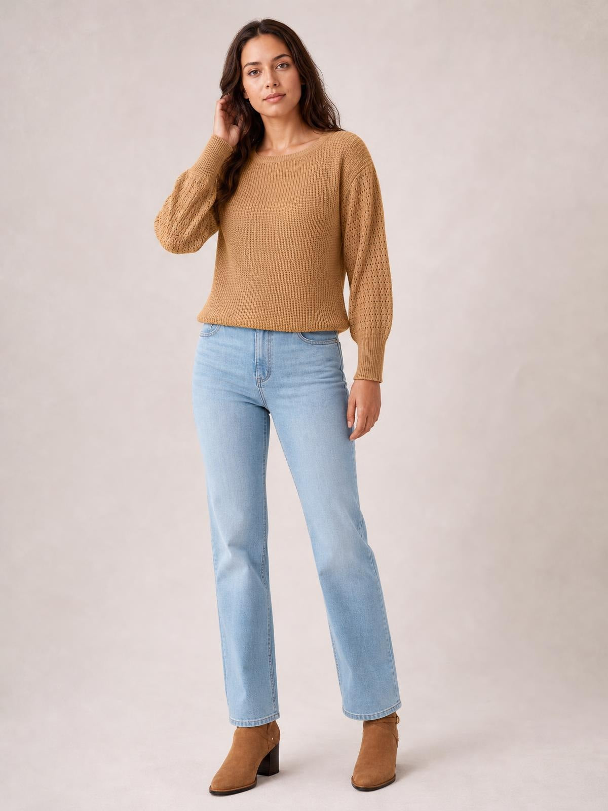 Model touches her hair while wearing a camel ribbed pullover sweater with a round neck, dropped shoulders, long openwork sleeves, and a regular silhouette.