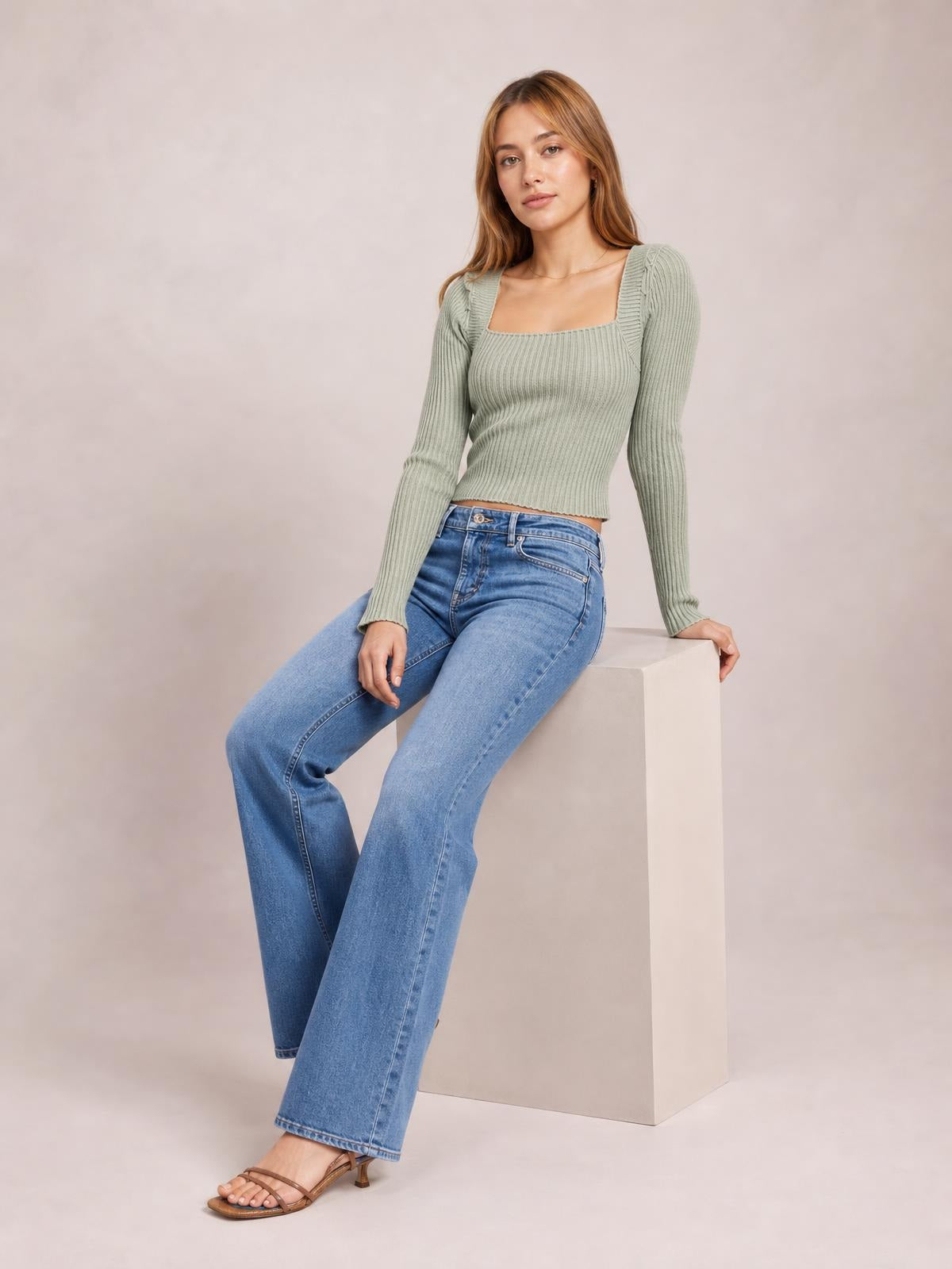 Model seated in a sage green ribbed square neck sweater with long sleeves, fitted silhouette, and subtle tied shoulder details.