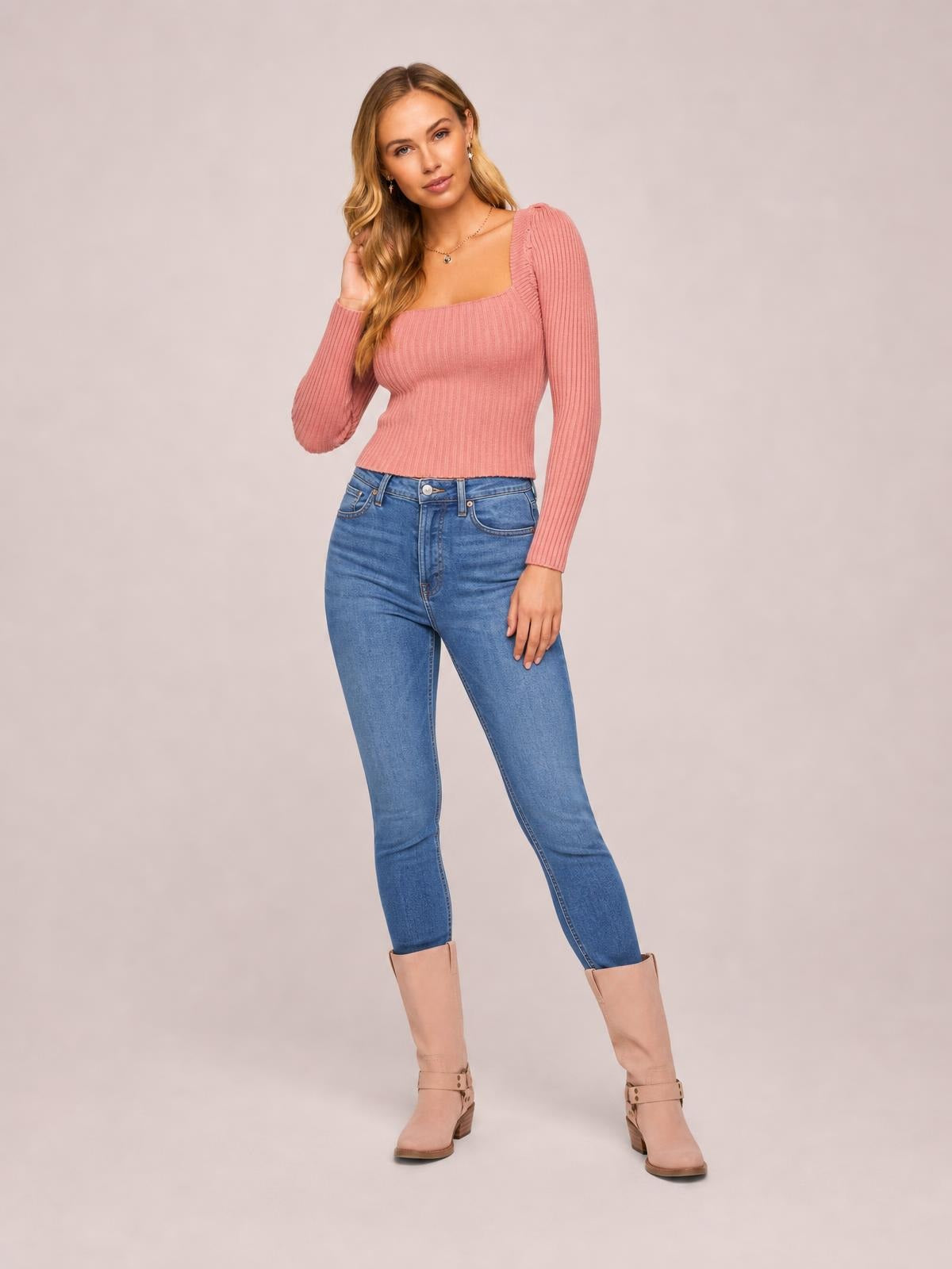 A woman poses in a pink ribbed square neck long sleeve sweater with a fitted waist-length silhouette and stretchy construction.