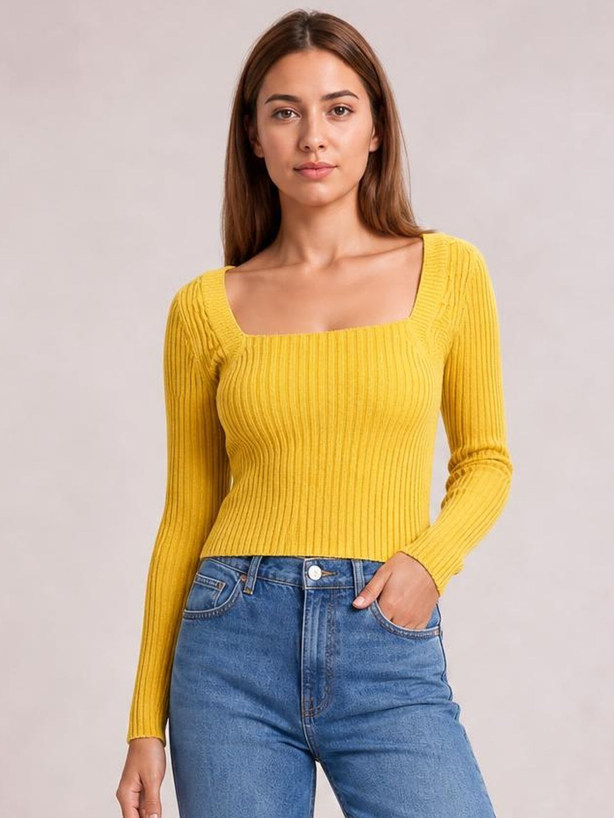 Model wearing a mustard yellow ribbed square neck long sleeve sweater with a fitted silhouette, standing with one hand in her jeans pocket.