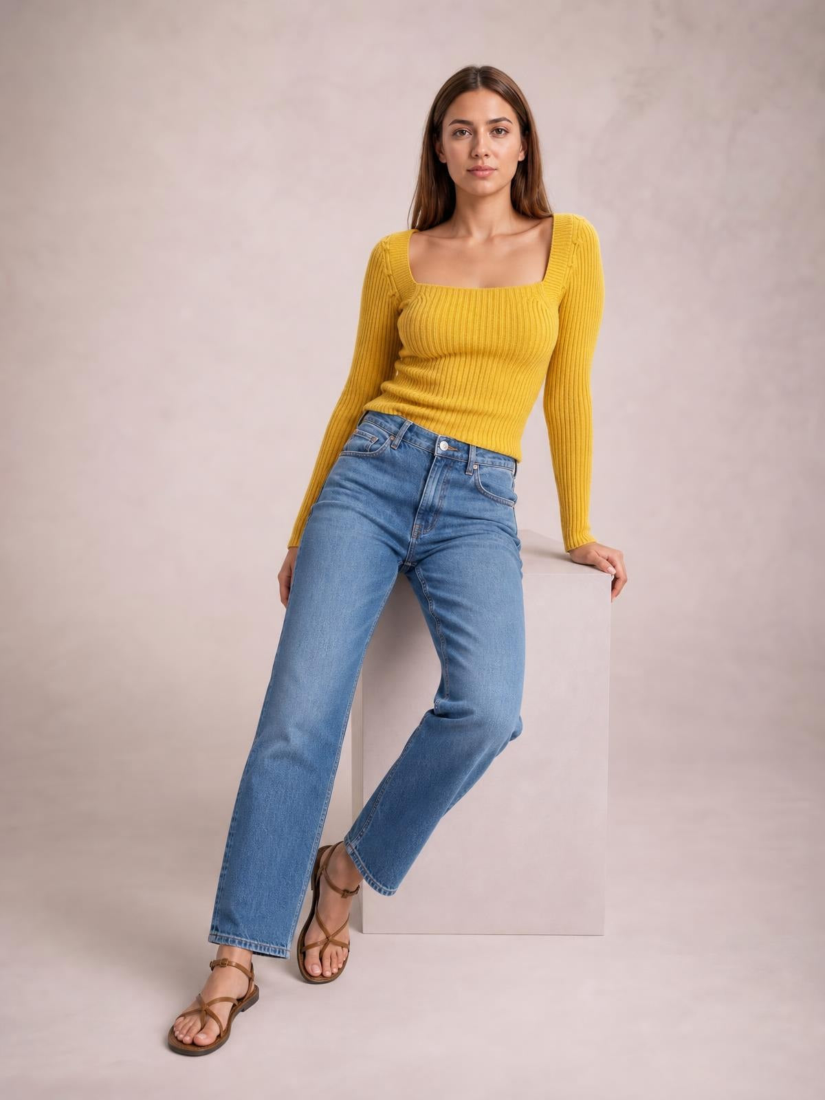 Model poses in a mustard yellow ribbed sweater with a square neckline, long sleeves, and a fitted stretchy silhouette styled with blue jeans.