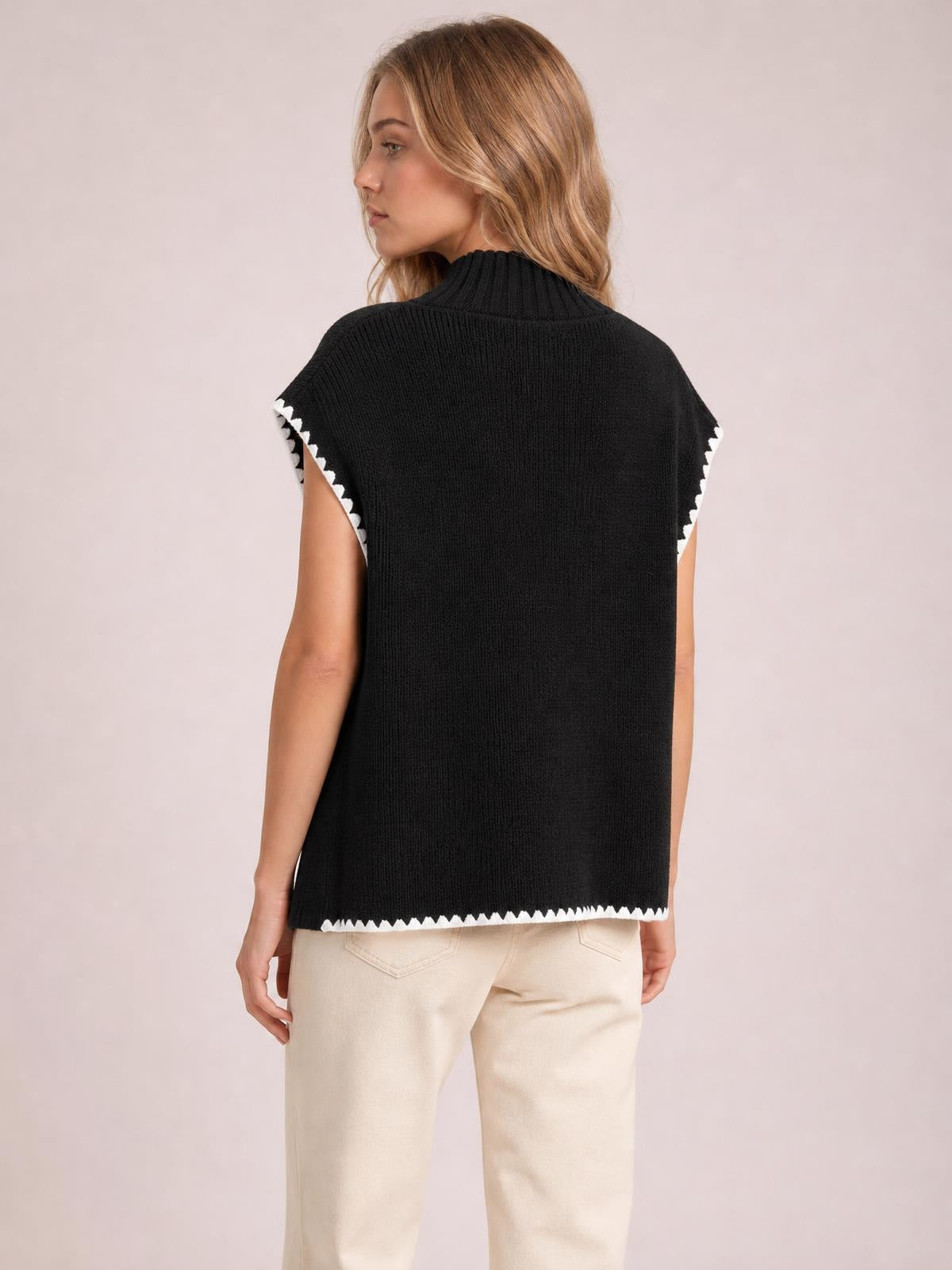 Model shown from behind in a black ribbed turtleneck sweater vest with white contrast trim, relaxed straight silhouette, and sleeveless construction.
