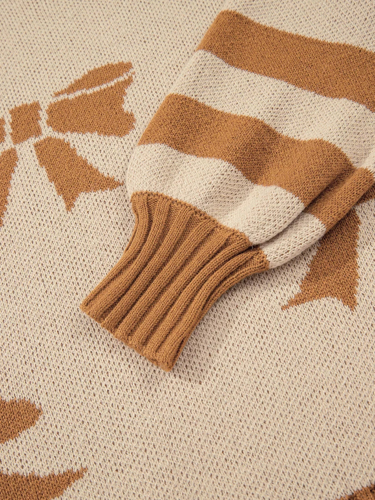 Close-up of a cream knit sweater with camel-brown ribbon bow, checkered and striped motifs, textured construction, and a ribbed cuff.