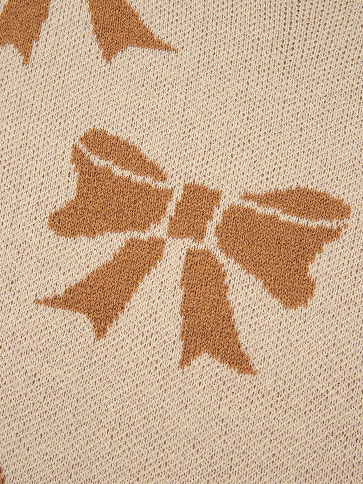 Close-up of a cream knit sweater featuring brown ribbon bow motifs, with visible textured stitching and a soft, slightly stretchy construction.