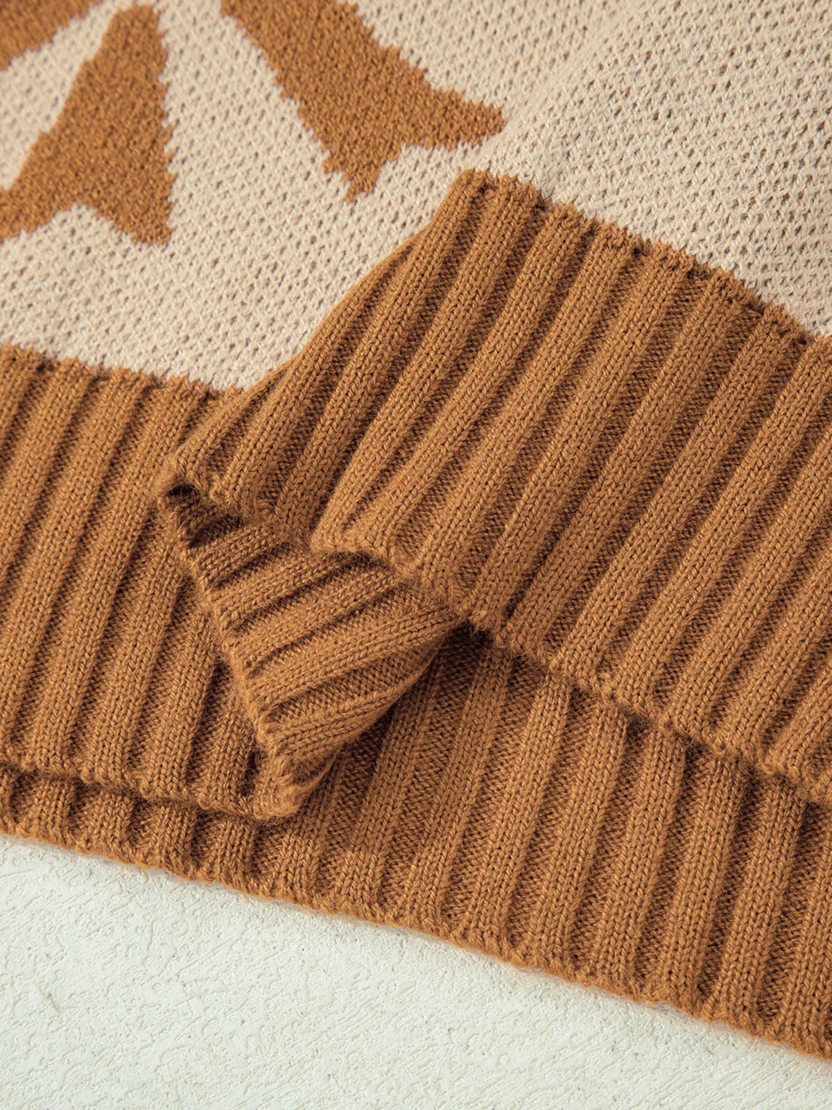 Close-up of a brown knit sweater showing ribbed striped fabric, a folded sleeve, and contrasting cream checkered detailing.