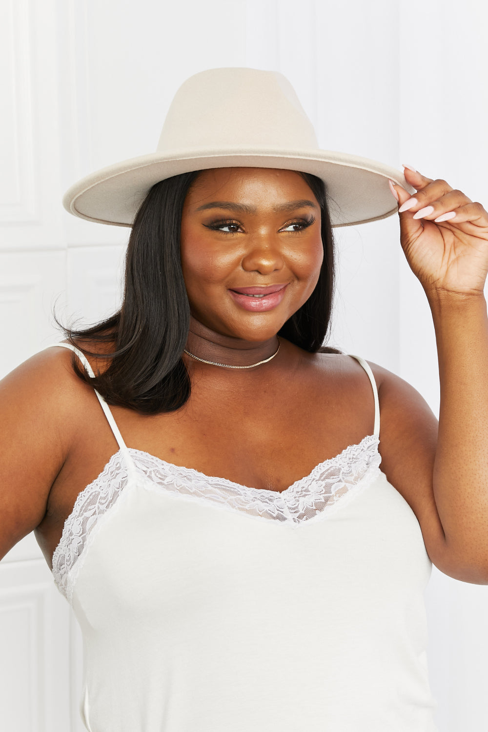 A smiling model holds the brim of the soft beige Ride Along fedora, showcasing its wide silhouette and clean, structured crown.