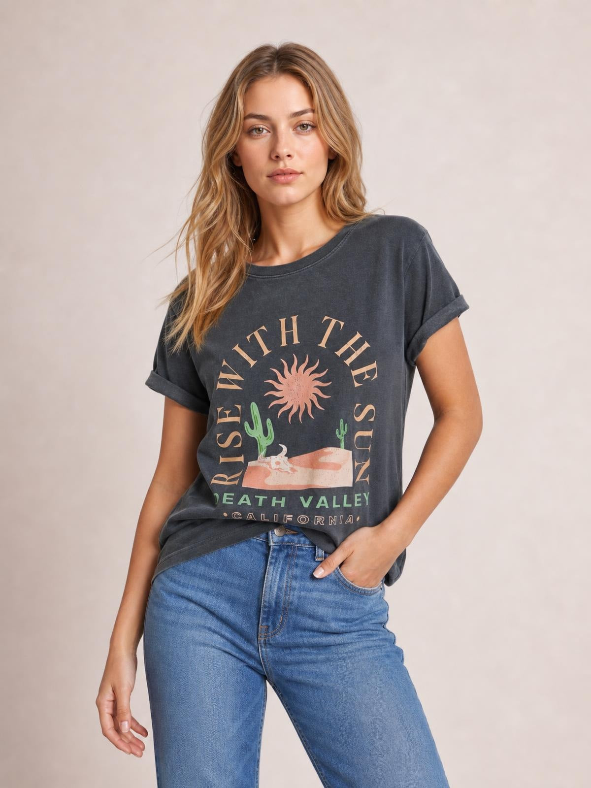 A model poses in a charcoal RISE WITH THE SUN graphic T-shirt with a round neck, rolled short sleeves, relaxed silhouette, and desert sun print.