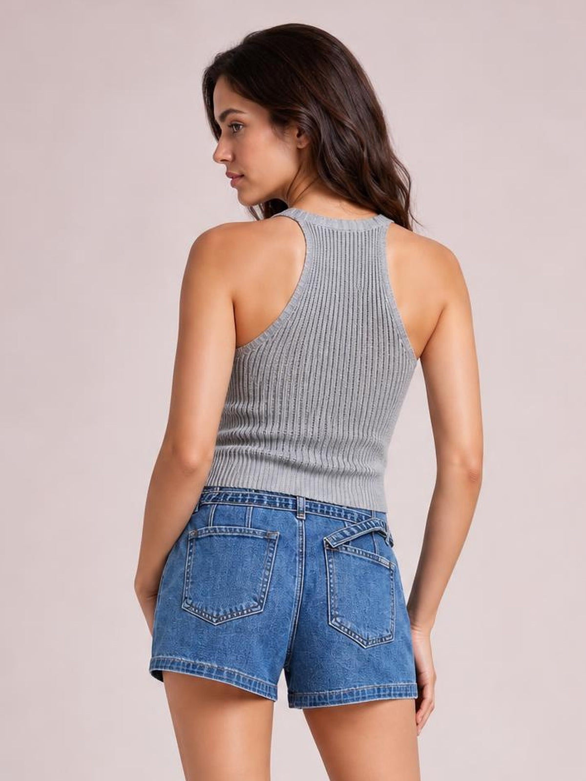A model poses from behind in blue denim slouchy shorts with a relaxed silhouette, stitched back pockets, belt loops, and a neatly finished hem.