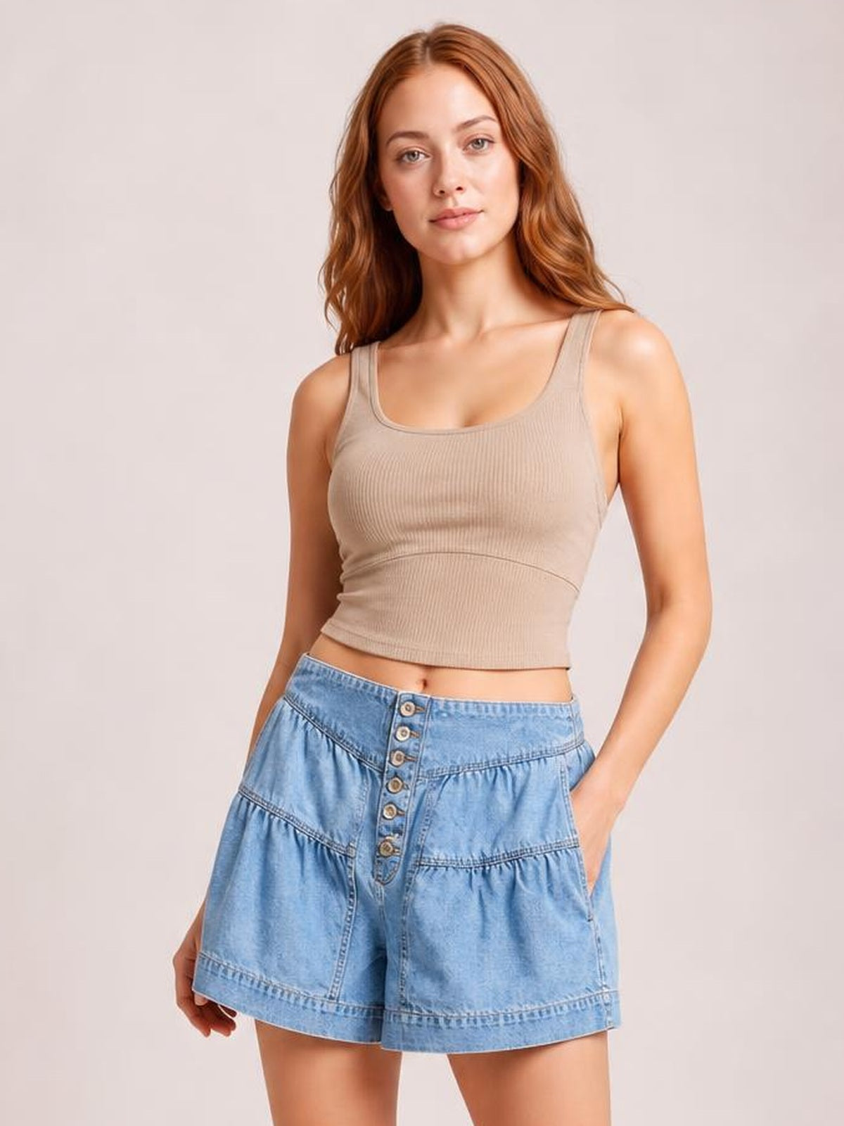 A model poses with one hand in a pocket, wearing light blue slouchy shorts with an elastic waistband, shirred panel detailing, loose legs, and a buttoned front.