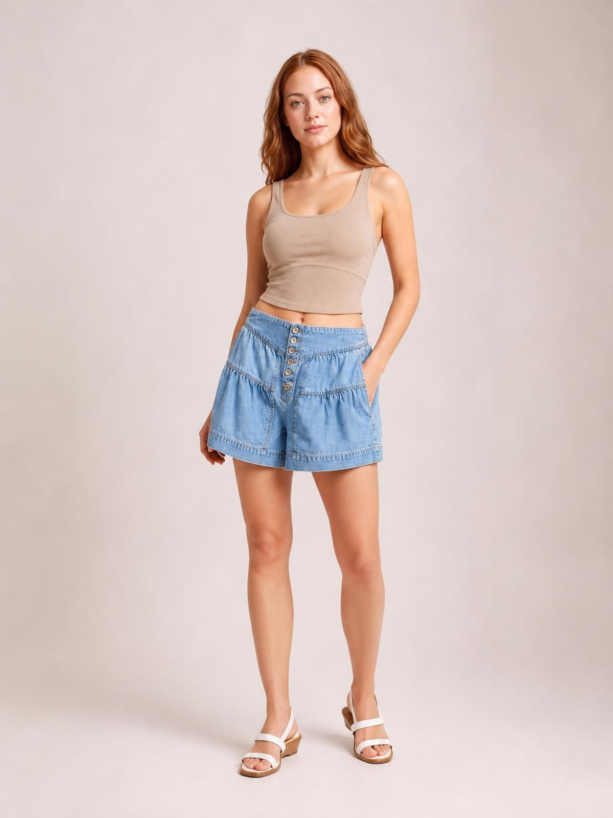 A model stands with one hand in a pocket, wearing light blue slouchy shorts with a shirred elastic waistband, front buttons, paneled construction, and a relaxed silhouette.