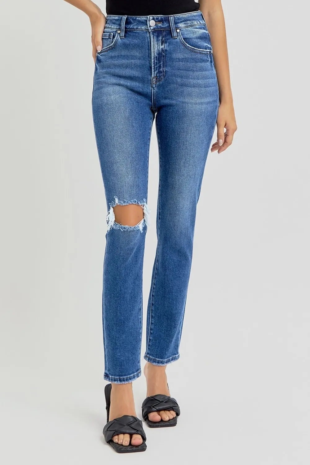 Model wearing blue washed high-rise skinny jeans with five-pocket construction, a button fly, knee distressing, and ankle-length hems, posing with one hand in a pocket.