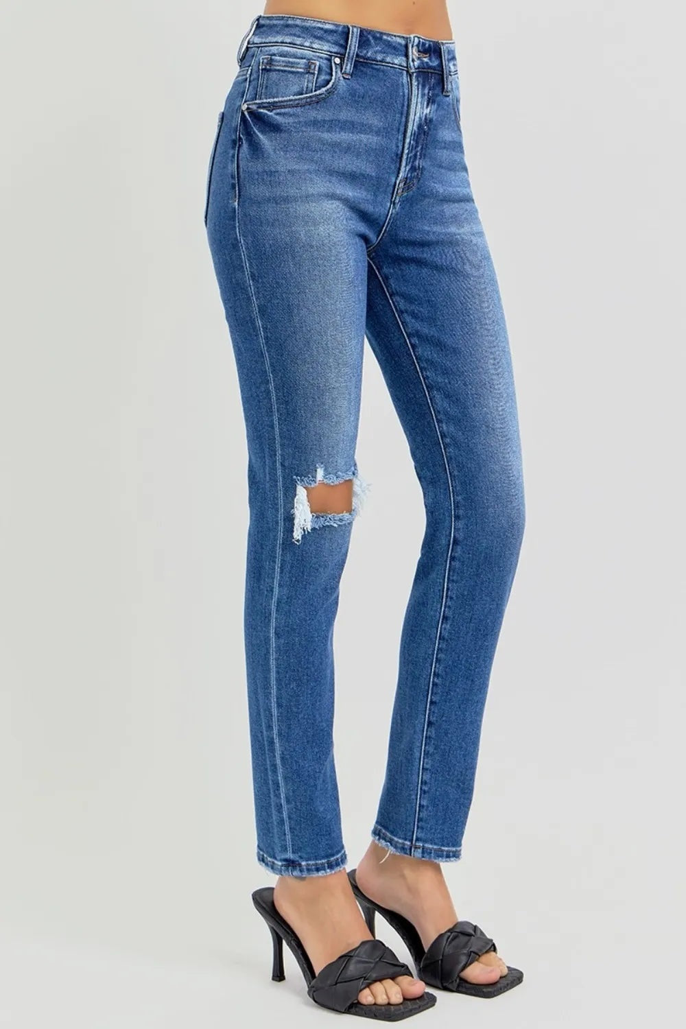 Model stands in blue high-rise ankle skinny jeans with a washed finish, pocketed construction, cropped hems, and distressed knee detailing.