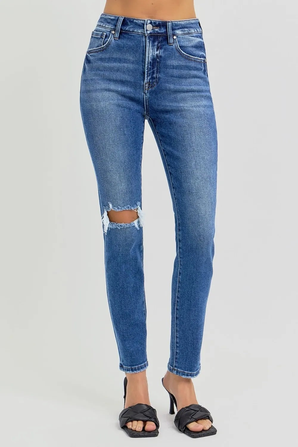 Model stands in blue washed high-rise ankle skinny jeans with five-pocket construction, a fitted silhouette, and prominent distressed knee detailing.
