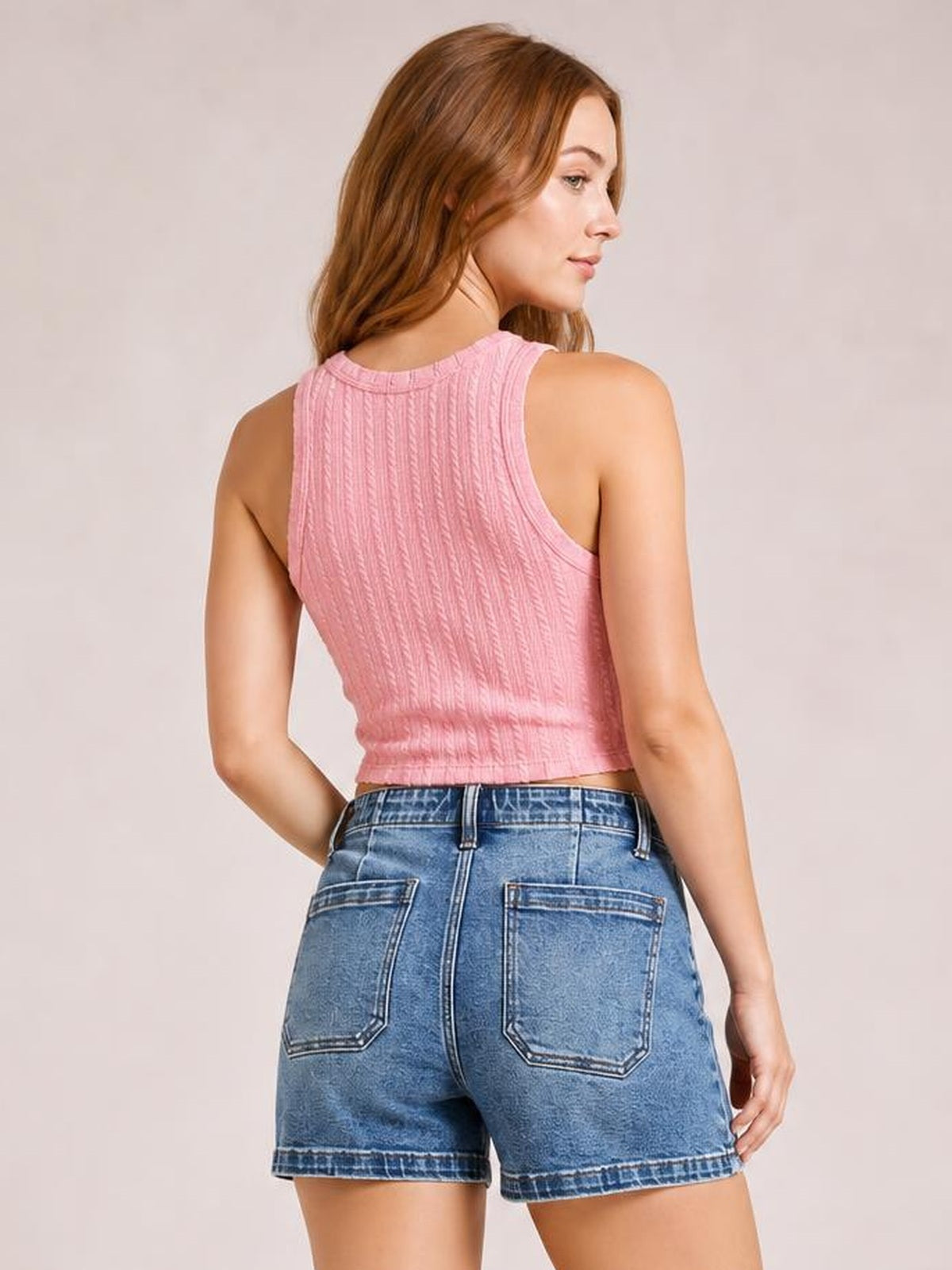 A model poses in blue high-rise denim shorts with a relaxed fit, rolled hems, belt loops, and large stitched patch pockets visible from the back.
