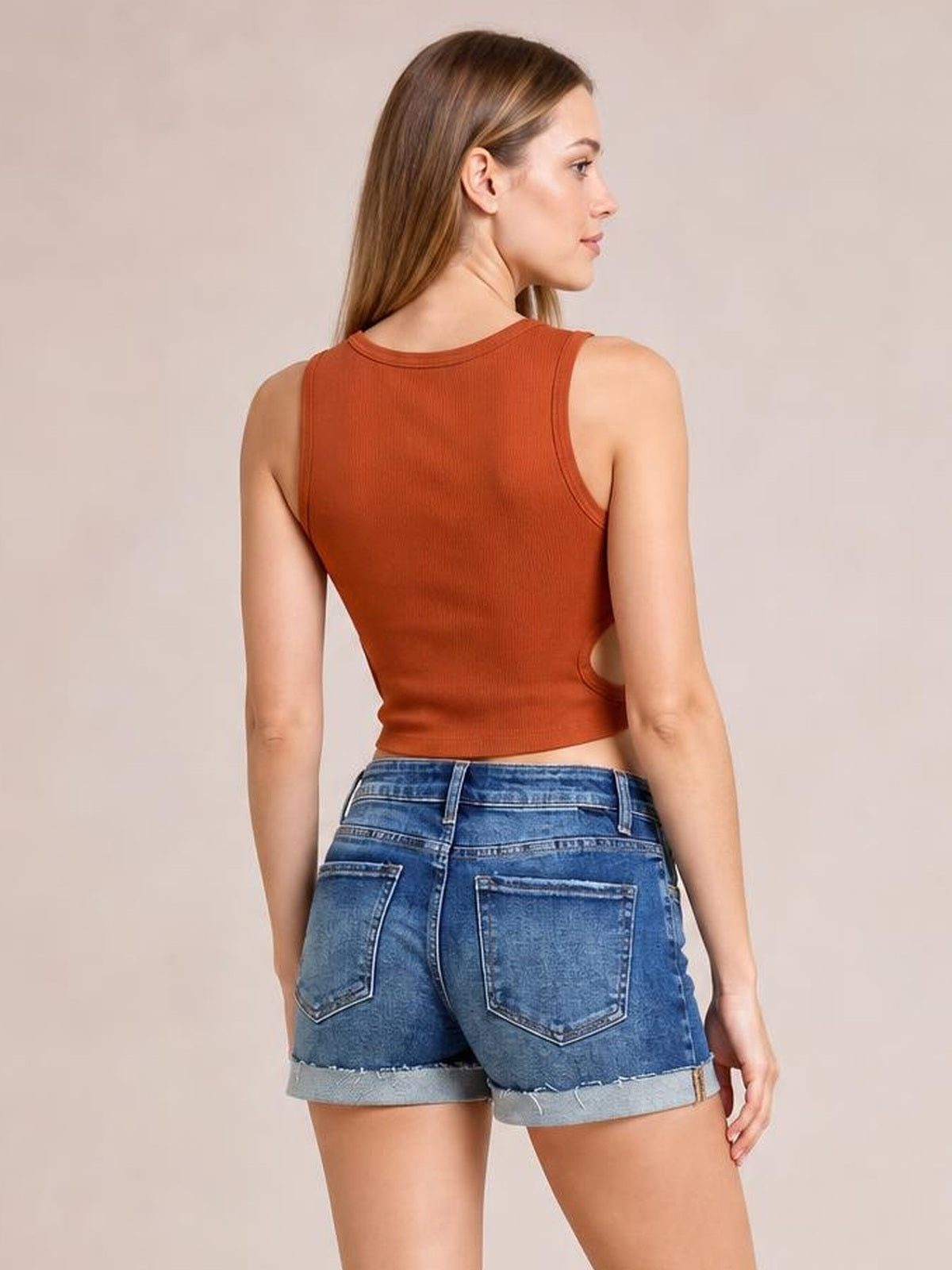 A model poses from the back in blue denim low-rise cuffed shorts with a relaxed silhouette, belt loops, patch pockets, and raw frayed hems.