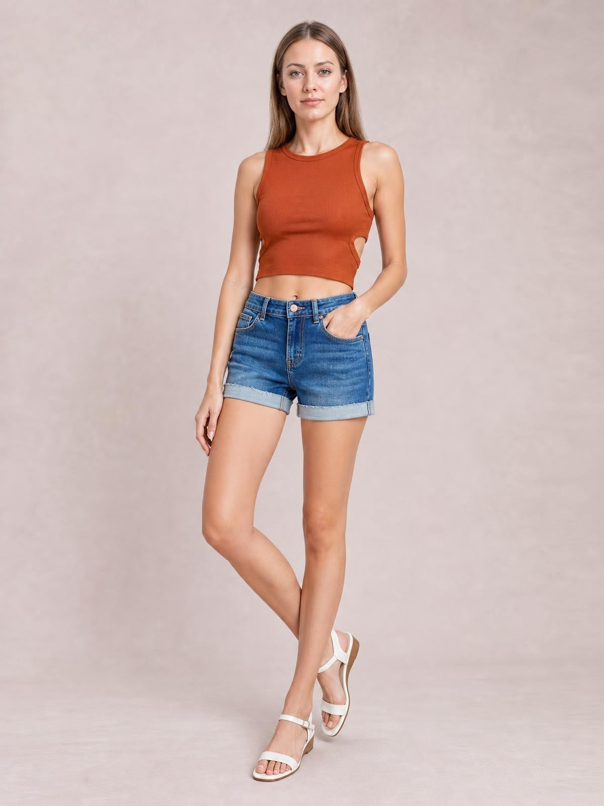 Model poses in blue low-rise denim shorts with rolled cuffed raw hems, five-pocket construction, and a relaxed silhouette.