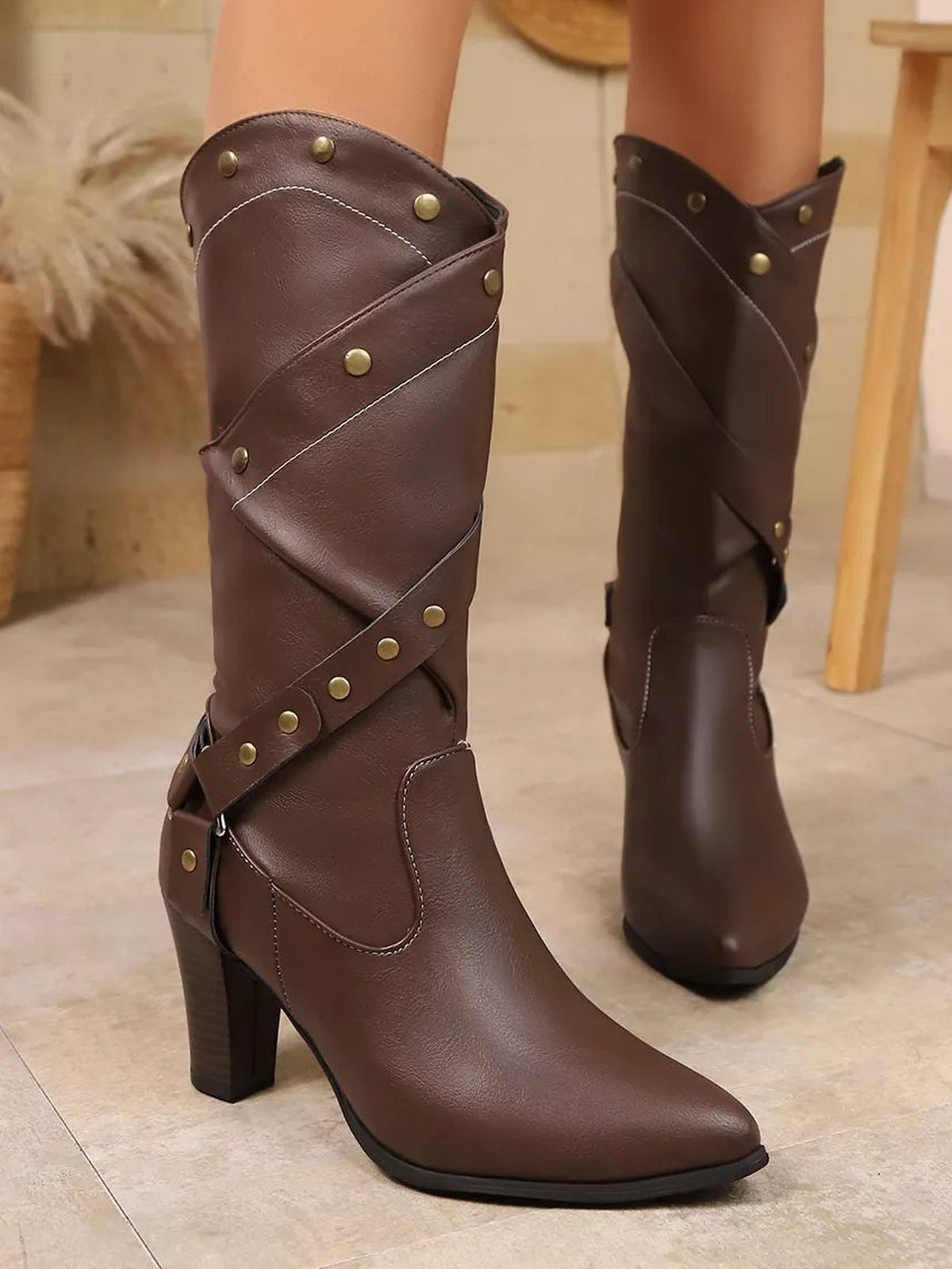 Brown PU leather high-heeled boots feature pointed toes, tall shafts, criss-cross straps with rivet details, and sturdy block heels.