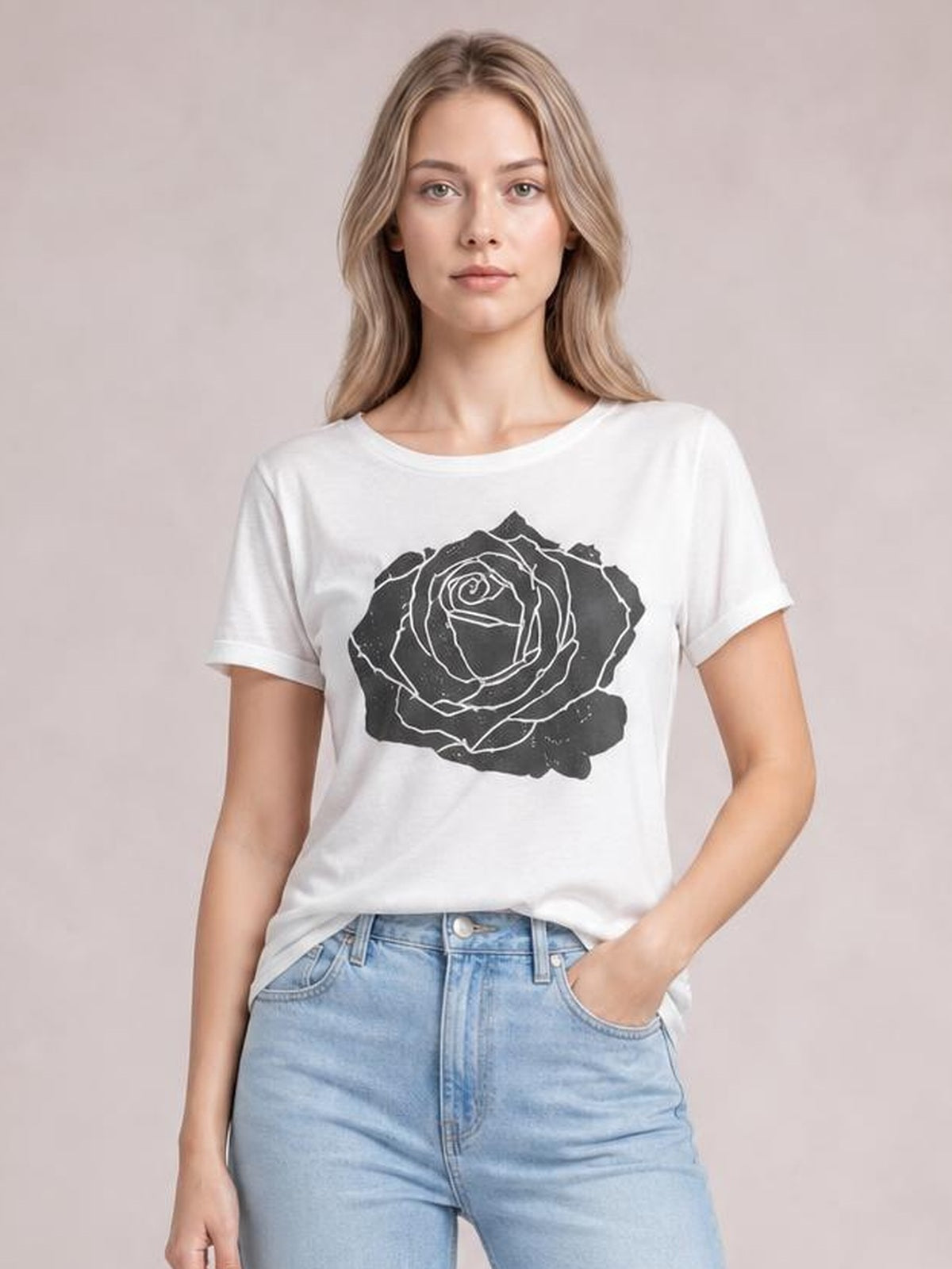 Model wears a white rose graphic round neck short sleeve T-shirt with a relaxed silhouette, shown front-facing with one hand in her jeans pocket.