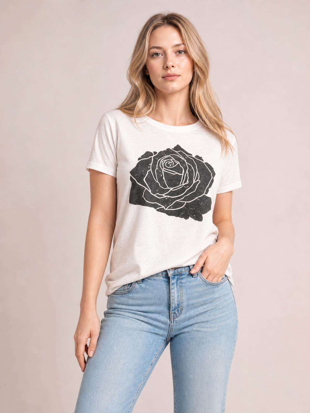 Model wearing an opaque white rose graphic round neck short sleeve T-shirt with a relaxed silhouette, paired with light-wash jeans and one hand in a pocket.