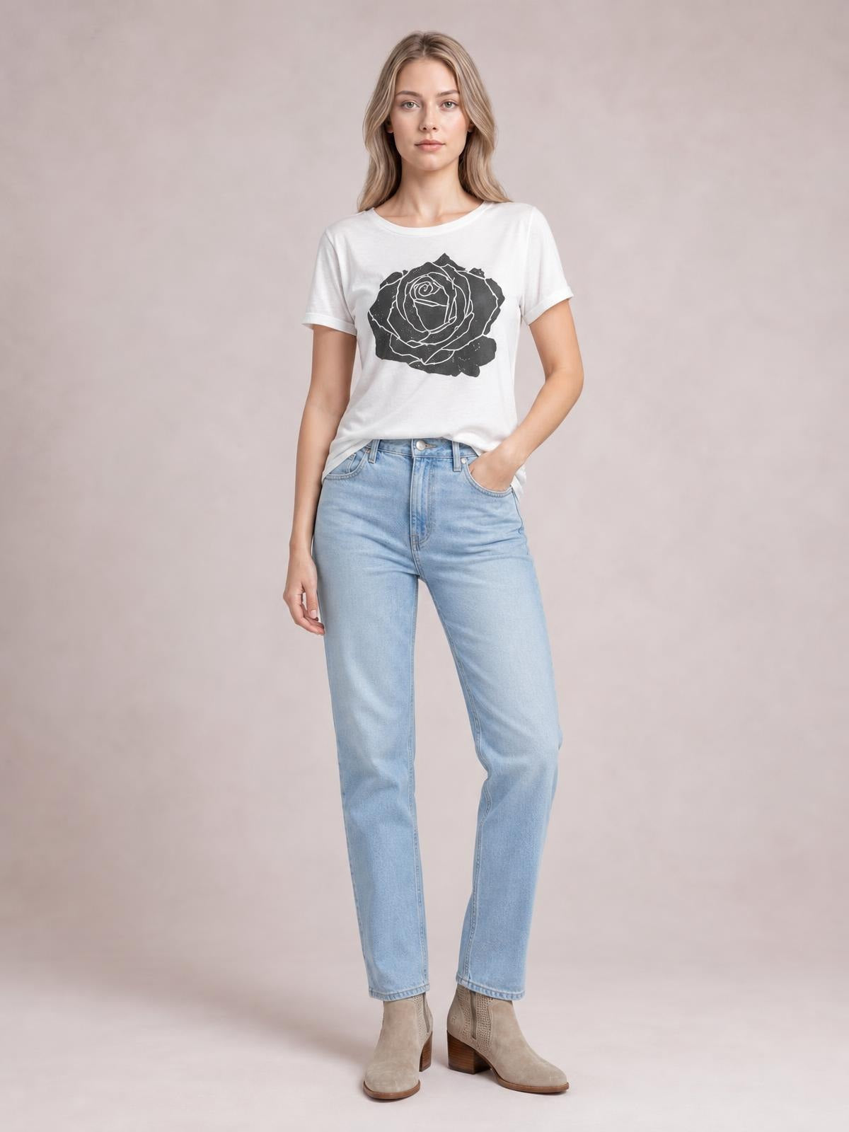 A model stands in a white round neck short sleeve T-shirt with a bold black rose graphic and relaxed silhouette, one hand tucked into her jeans pocket.
