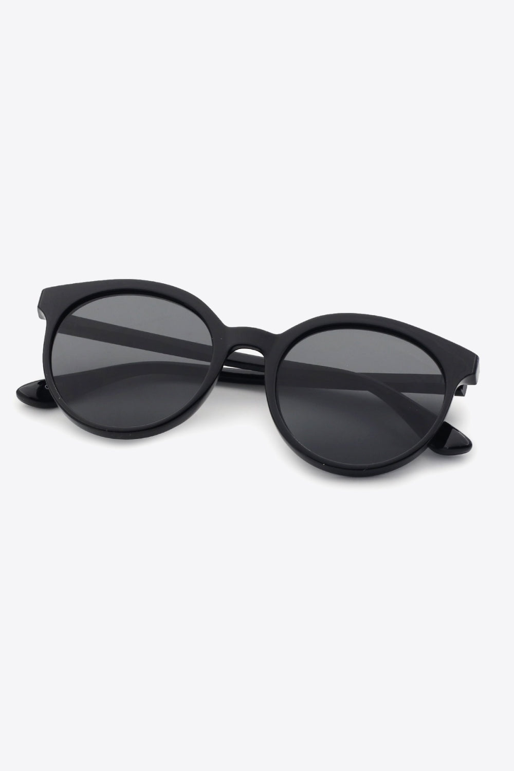 Black round full-rim polycarbonate sunglasses feature softly curved frames, dark acetate lenses, a defined bridge, and folded temples for a polished everyday silhouette.