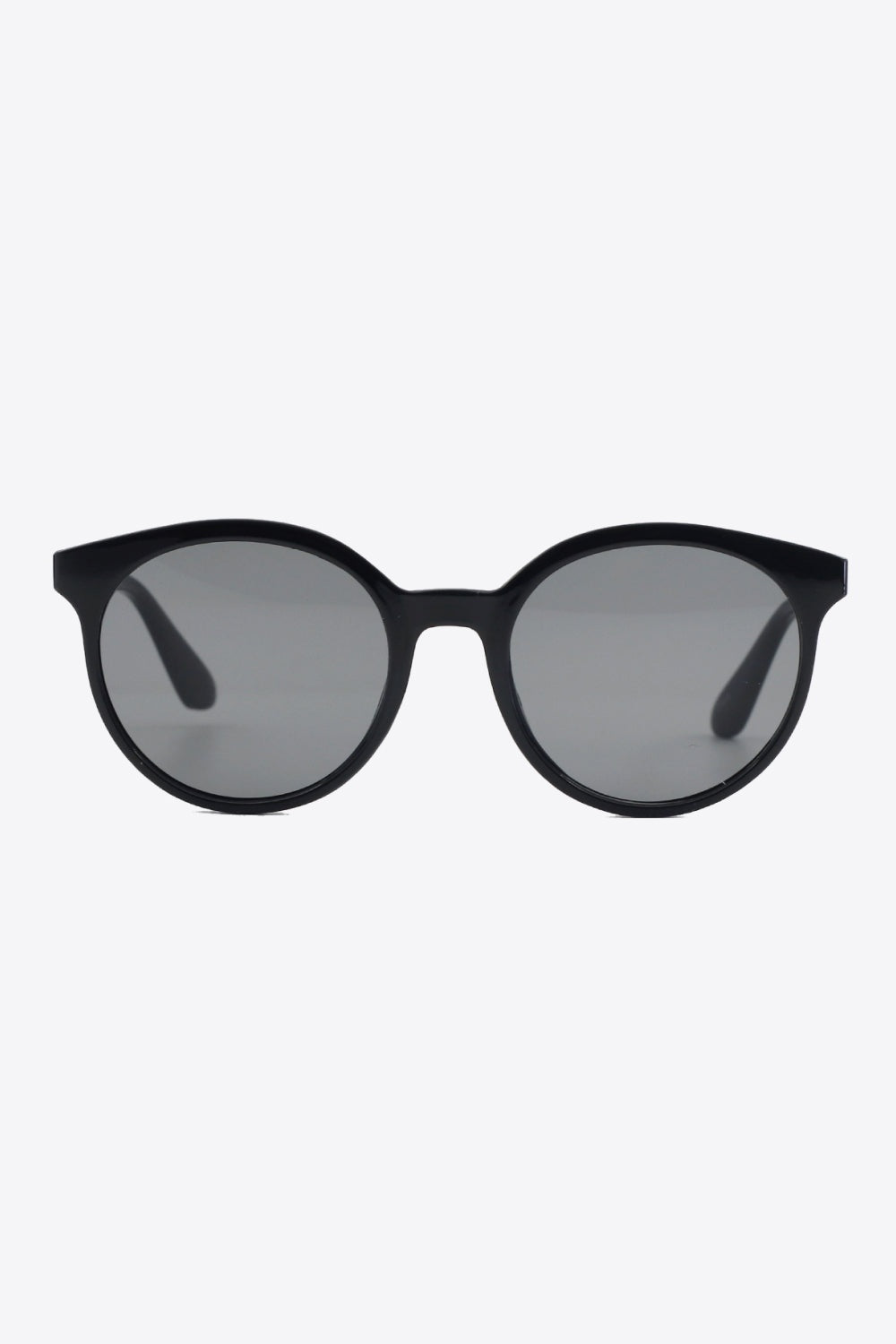 Black round full-rim polycarbonate sunglasses feature a softly curved silhouette, polished frame, gray acetate lenses, and sturdy temples visible from the front.