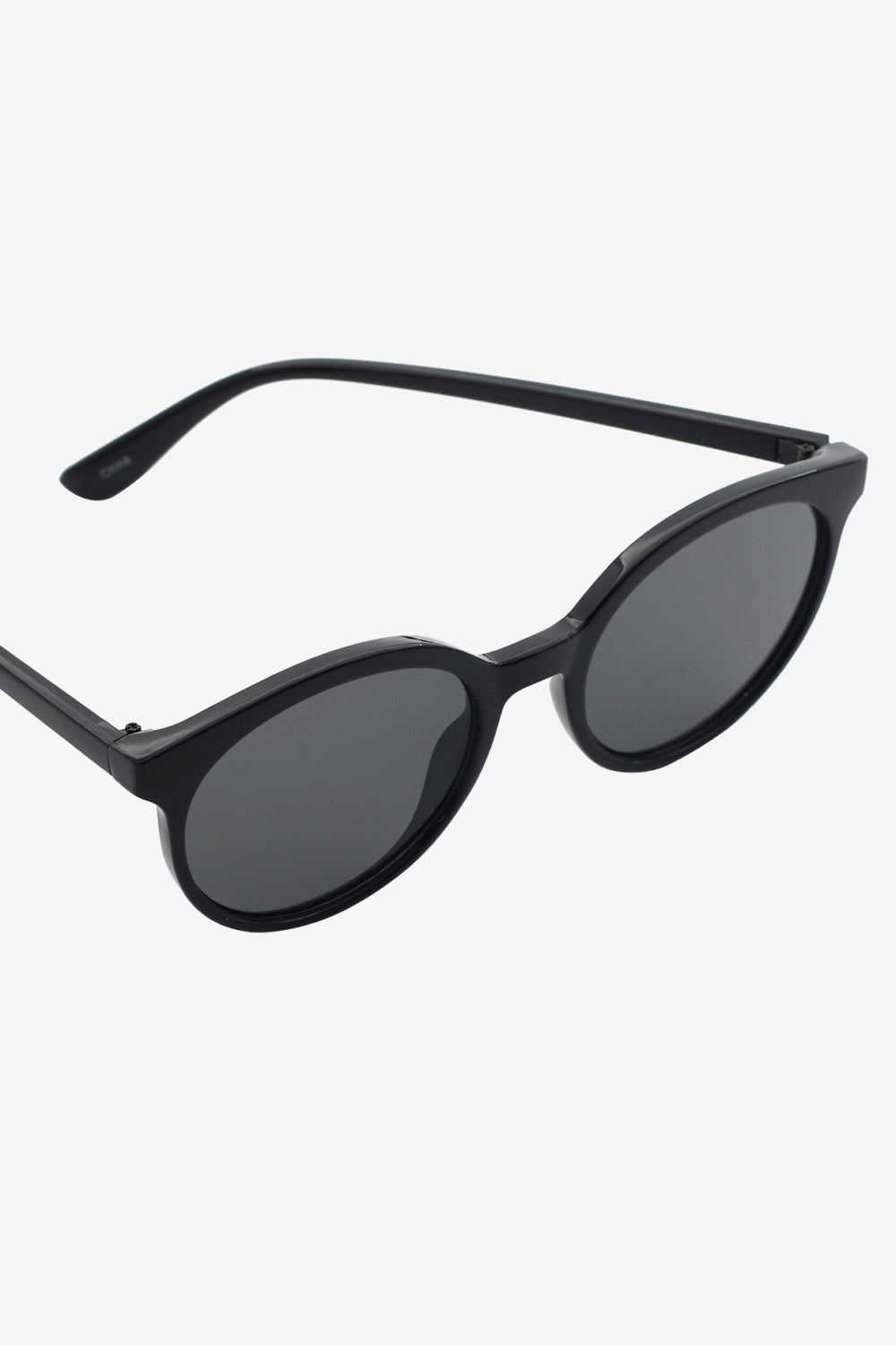 Black round full-rim polycarbonate sunglasses with dark acetate lenses, shown at an angled view with one temple extended to highlight the curved silhouette.