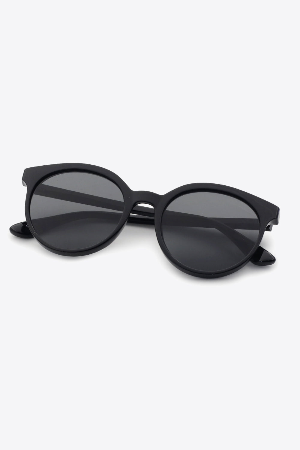 Black round full-rim polycarbonate sunglasses feature softly curved frames, dark acetate lenses, a defined bridge, and folded temples for a polished everyday silhouette.