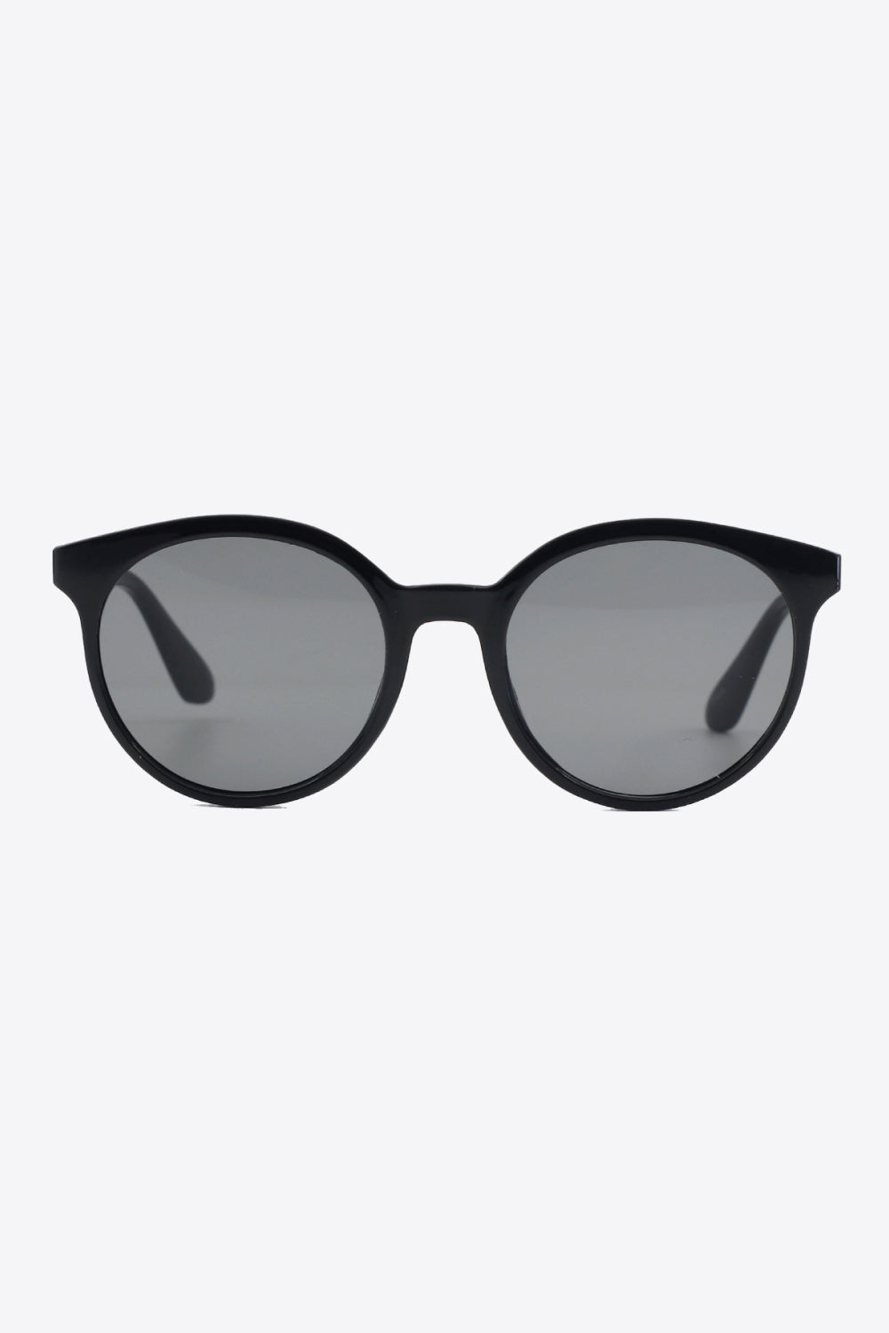 Black round full-rim polycarbonate sunglasses feature a softly curved silhouette, polished frame, gray acetate lenses, and sturdy temples visible from the front.
