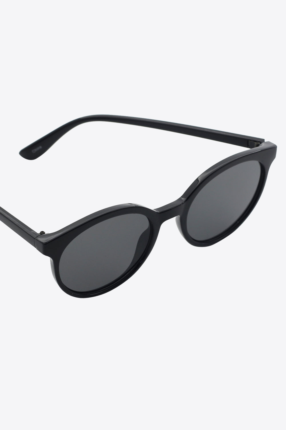 Black round full-rim polycarbonate sunglasses with dark acetate lenses, shown at an angled view with one temple extended to highlight the curved silhouette.