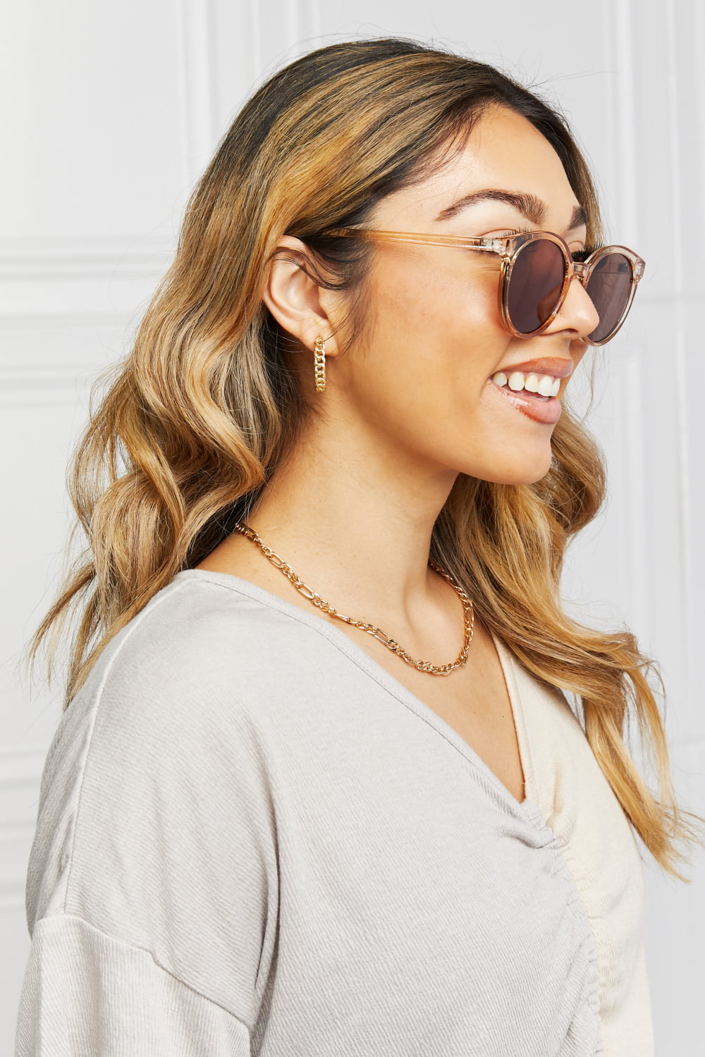 A smiling model in side profile wears round full-rim sunglasses with translucent amber polycarbonate frames, brown lenses, and slim temples.