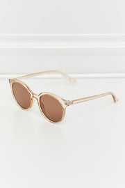 Round full-rim sunglasses in translucent peach polycarbonate feature softly curved brown lenses and slim temples, angled to showcase their polished construction.