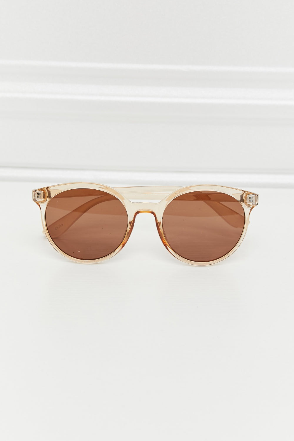 Round full-rim sunglasses feature a softly curved translucent amber polycarbonate frame with brown acetate lenses and matching structured temples.