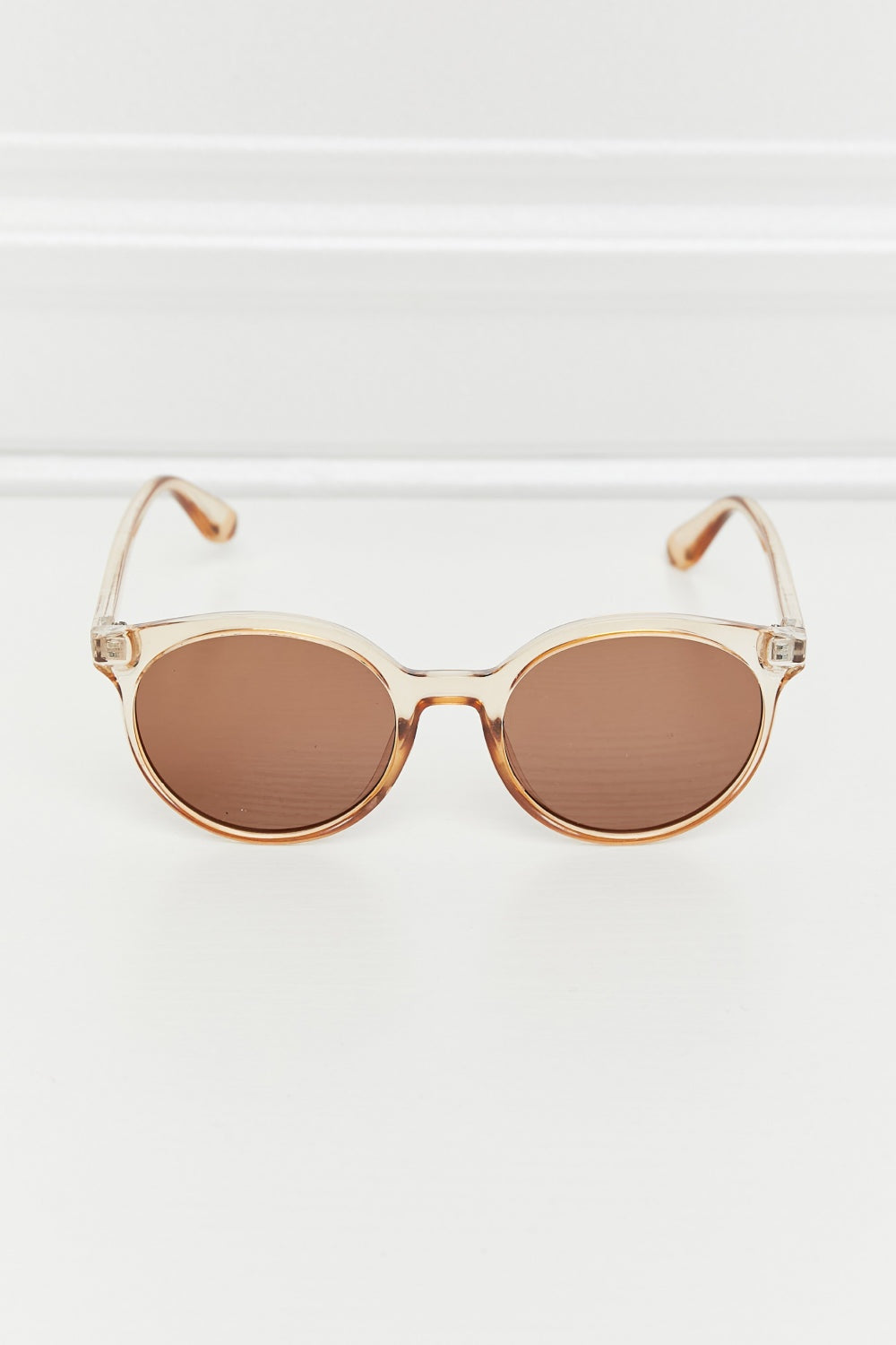 Round full-rim sunglasses feature a softly curved translucent amber polycarbonate frame, warm brown acetate lenses, a defined bridge, and slim temples.