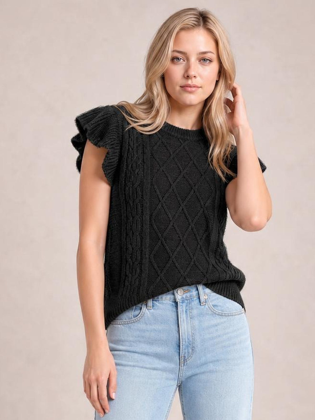 Model wearing a black round neck cap sleeve sweater with ruffled edges, cable-knit diamond and braided detailing, and a relaxed straight silhouette.