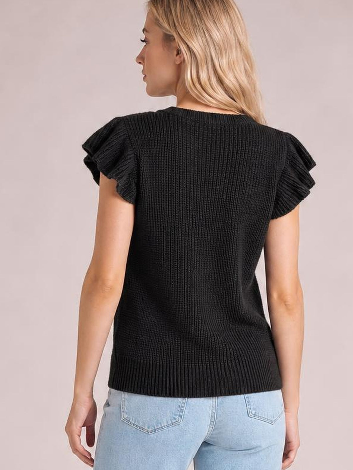 Model shown from the back wearing a black round-neck cap-sleeve sweater with ruffled sleeves, cable-knit texture, and a relaxed silhouette.
