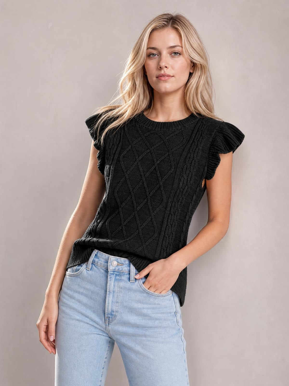 Model wearing a black round-neck cap-sleeve sweater with ruffled shoulders, cable-knit texture, and a relaxed silhouette, posing with one hand in her jeans pocket.
