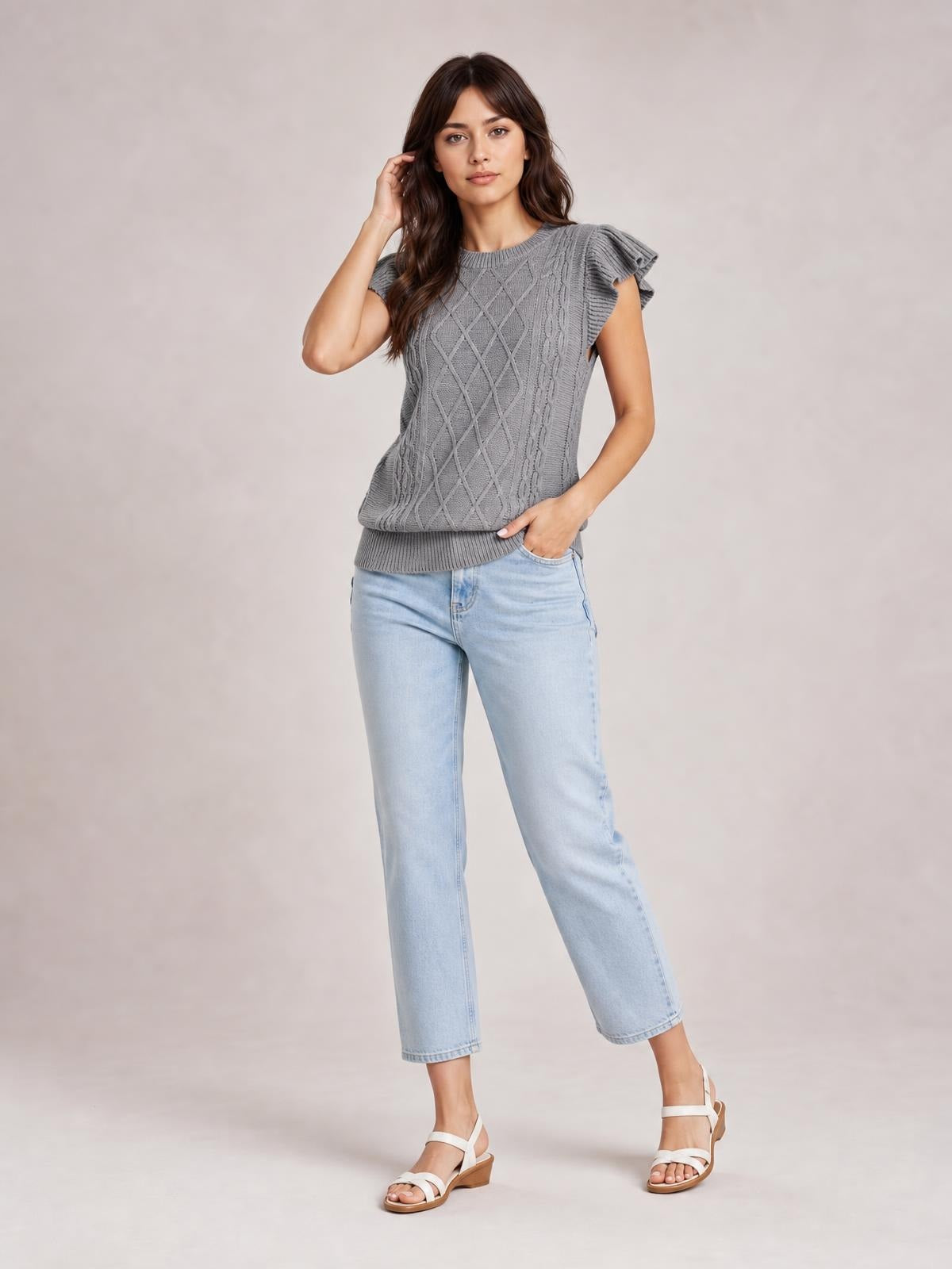 Model poses in a gray round neck cable-knit sweater with ruffled cap sleeves, ribbed trim, and a relaxed straight silhouette.