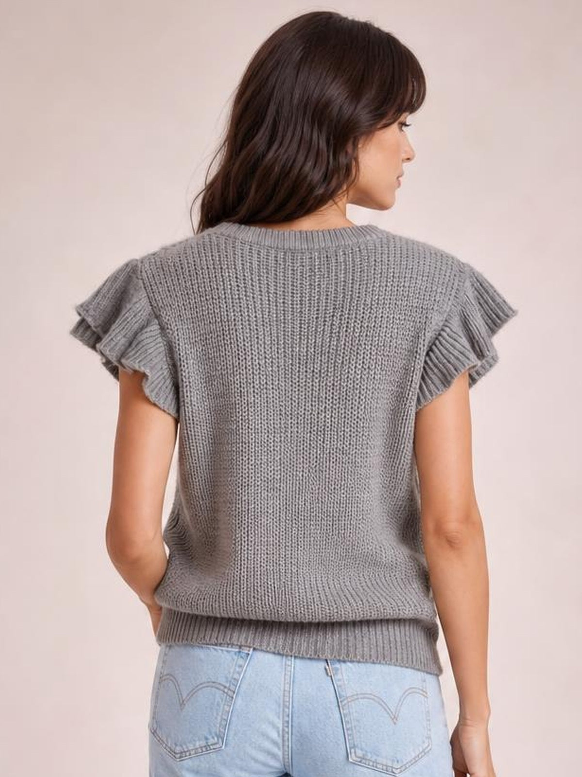 A model shows the back of a gray round-neck cap-sleeve sweater with ruffled edges, cable-knit texture, and a relaxed straight silhouette.