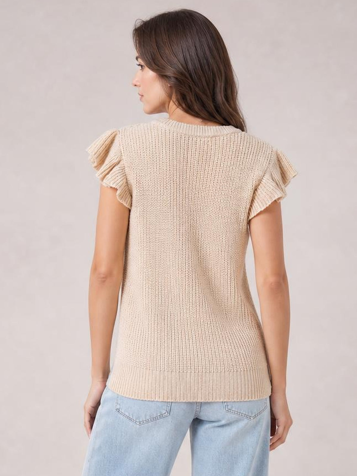 A model stands in a back view wearing a cream round-neck cable-knit sweater with ruffled cap sleeves, ribbed trim, and a relaxed straight silhouette.