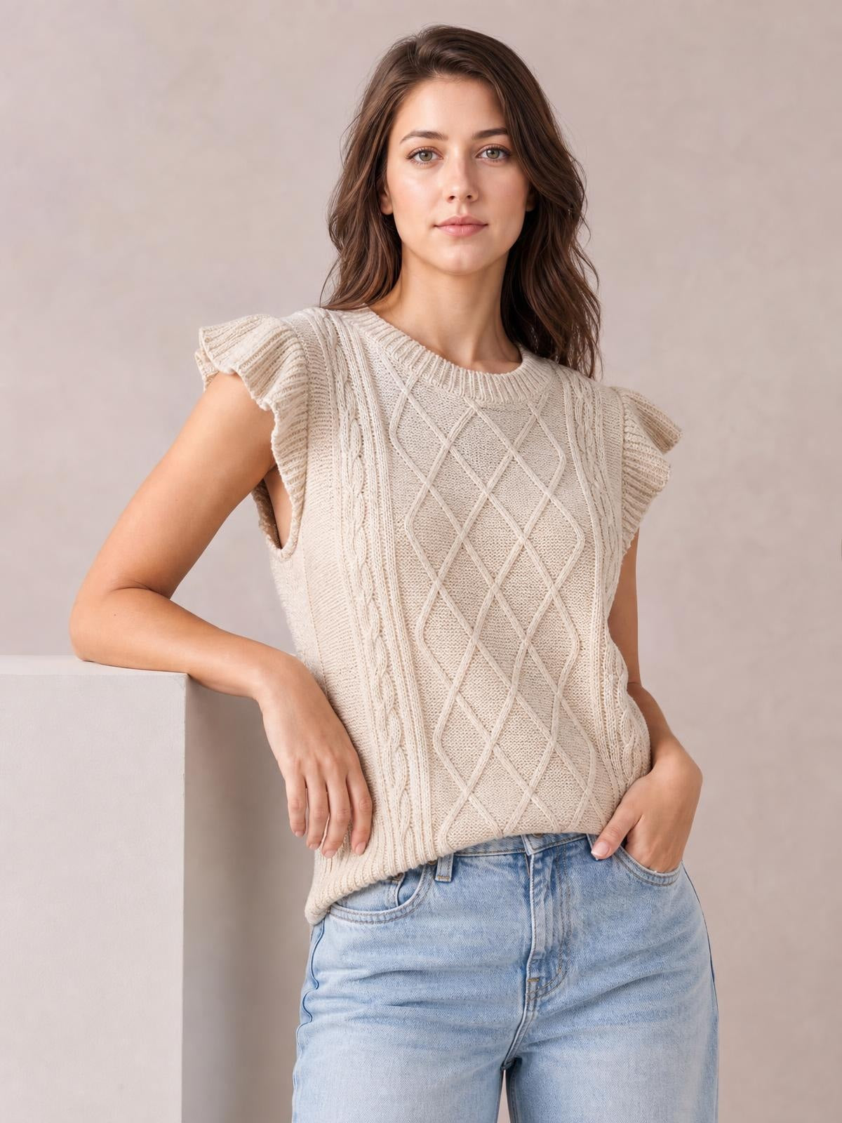 Model poses in a cream round-neck cap-sleeve sweater with ruffled edges, cable-knit diamond pattern, and a relaxed straight silhouette.